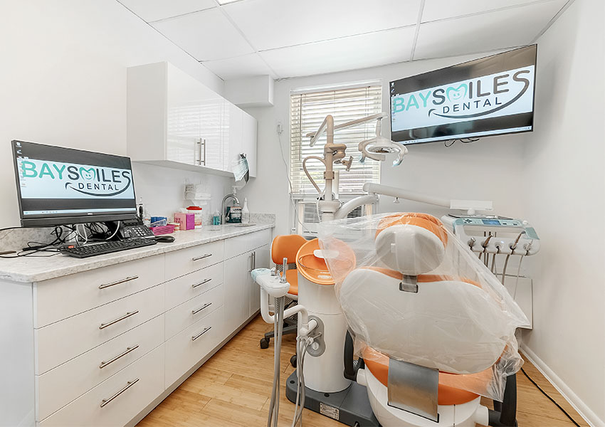 The image shows a dental office interior with a modern chair setup, a computer monitor displaying the logo of  Bay Smiles Dental,  and various dental equipment visible.