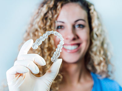 A woman in a blue shirt is holding up a transparent toothbrush-shaped object with a smile, against a white background.