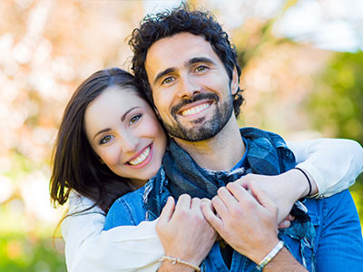 A man and a woman are embracing each other in an outdoor setting.