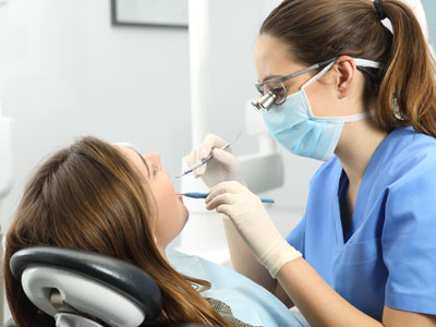 A dental hygienist assisting a patient during a teeth cleaning appointment, with both wearing protective masks and gloves.