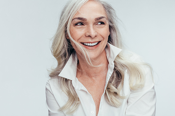 A woman with short hair and a smile, dressed in a white top, poses against a light background.