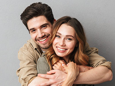 A man and woman are embracing each other, smiling warmly at the camera.