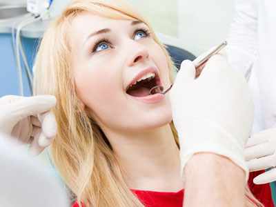 A young woman receiving dental care, with a dentist performing a procedure while she smiles and appears relaxed.